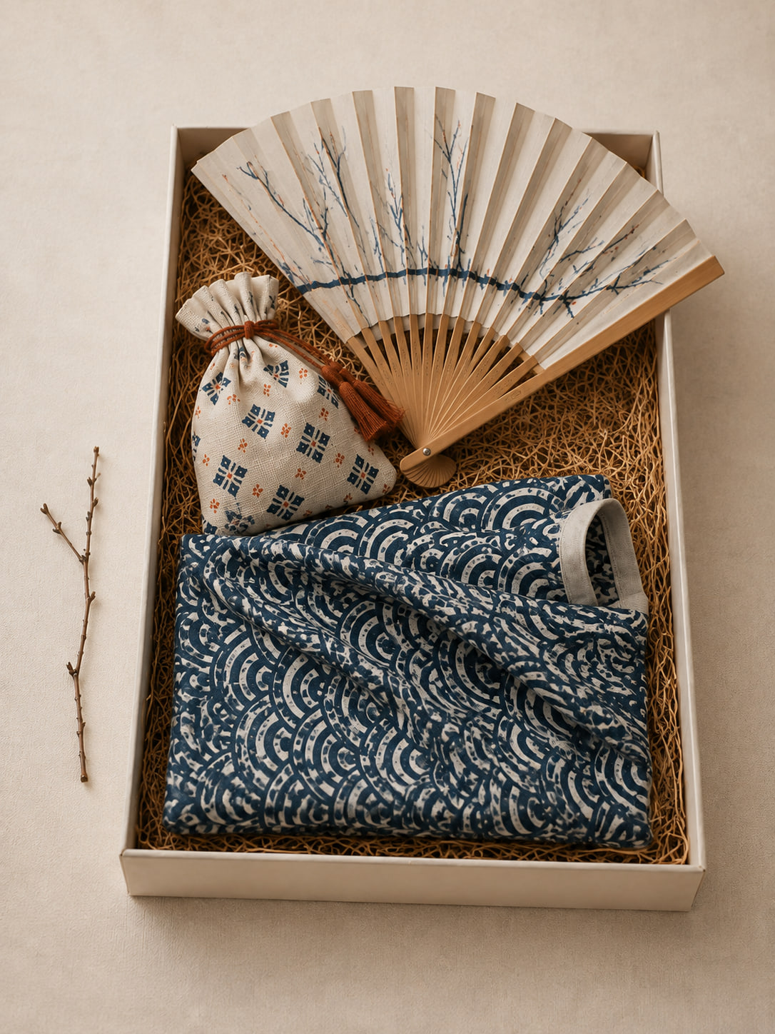 An open Kyoto box on linen — indigo wave-pattern tenugui, a drawstring incense sachet and a bamboo folding fan painted with plum branches